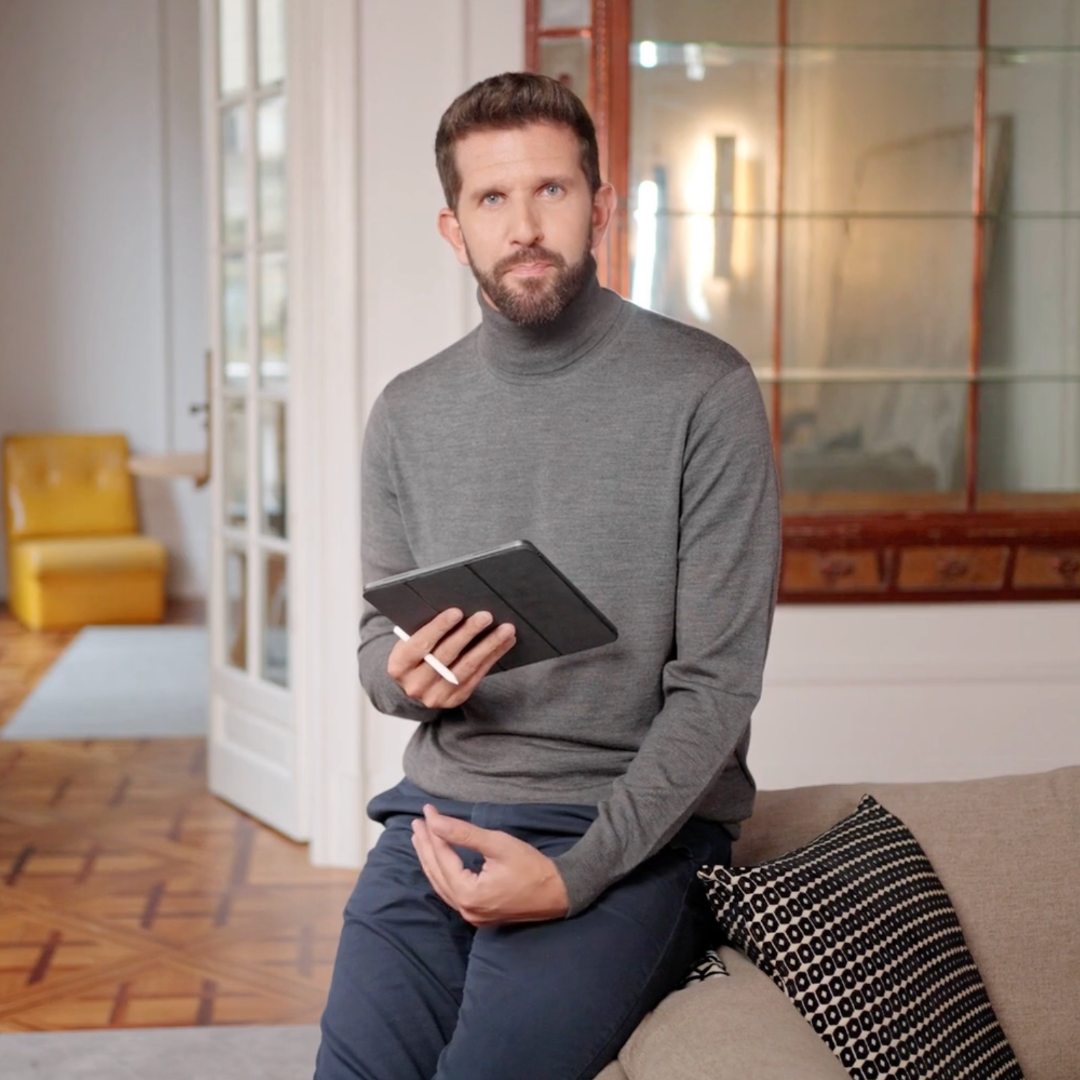 Man sitting on a couch holding a tablet in a living room.
