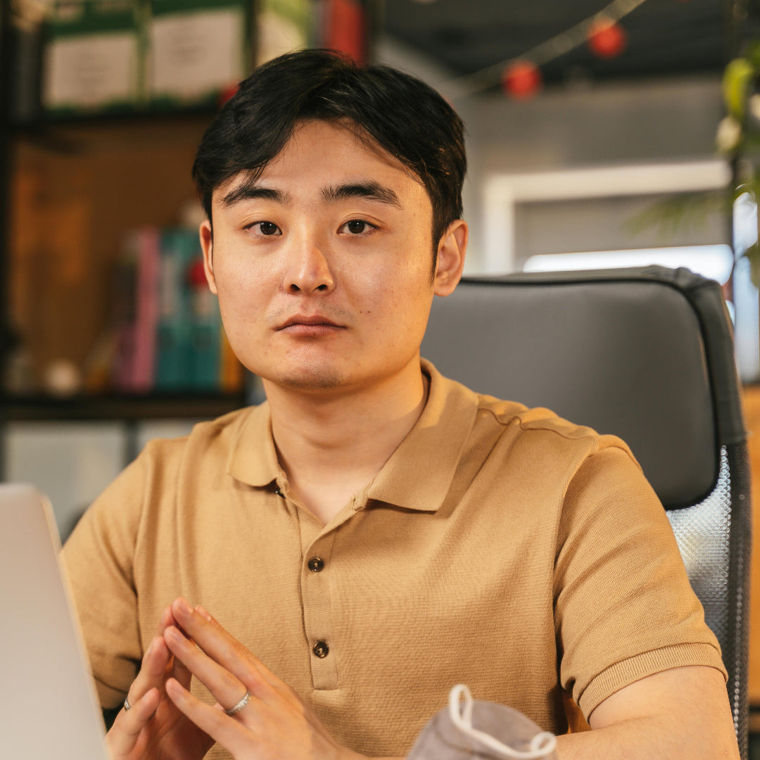 Man sitting at a desk with a laptop, wearing a beige polo shirt.