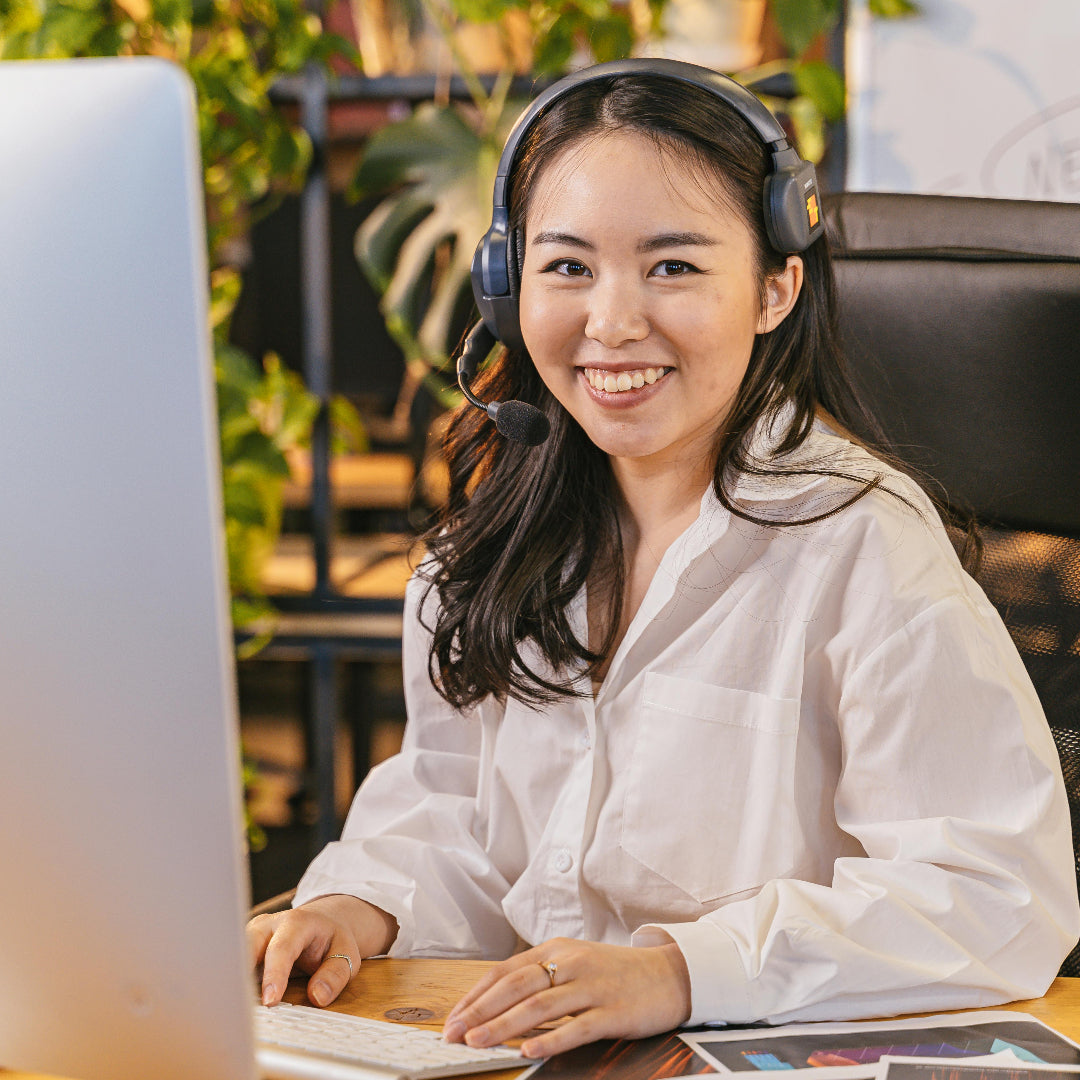 Woman wearing headphones and smiling at a computer desk in an office setting