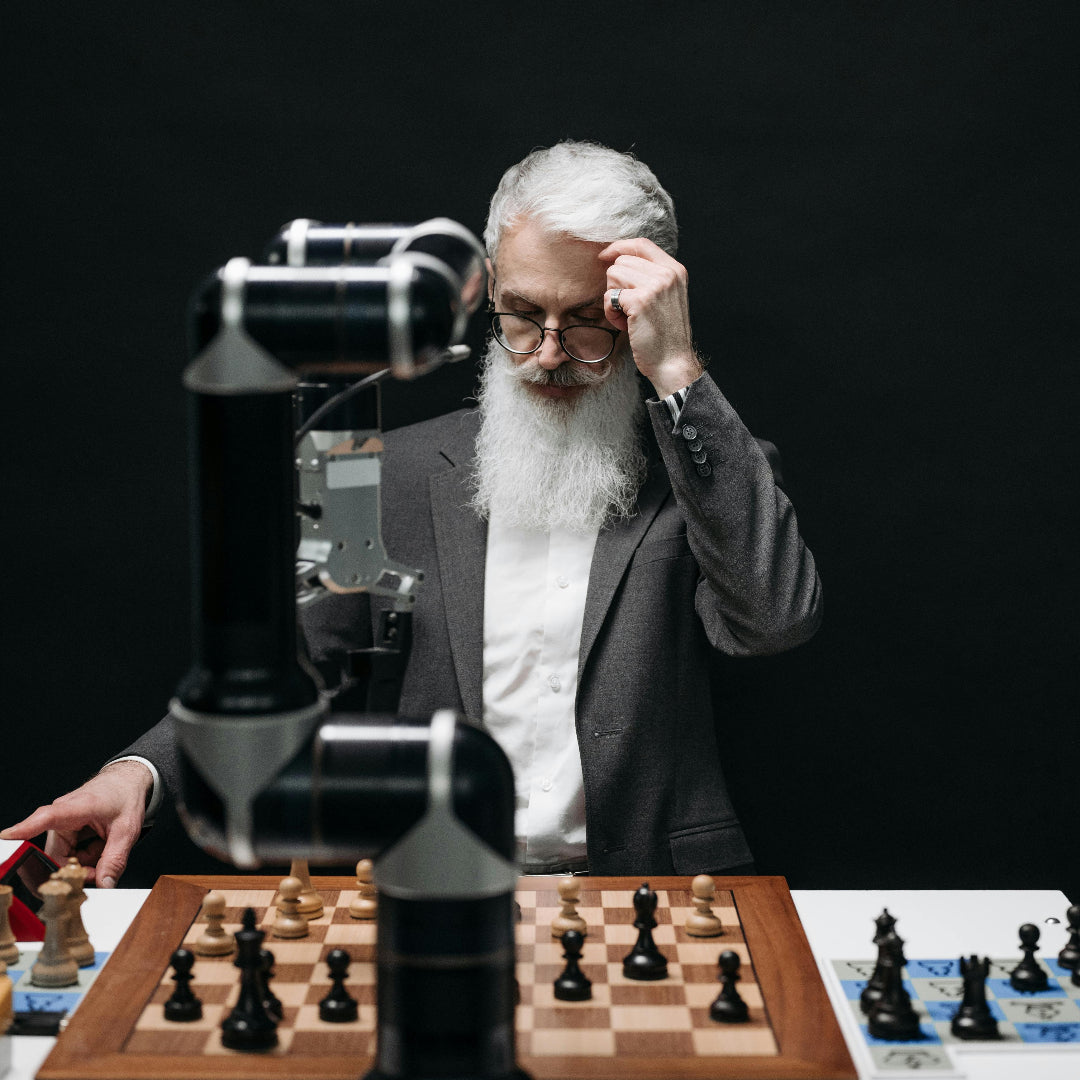 Man with a beard and glasses playing chess against a robot, with a black background.